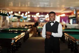 Young Handsome African Man Wearing White Shirt Black Vest Bow Tie Standing Against Pool Billiard Tables